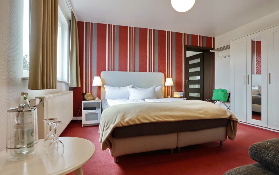 Schlafzimmer der Suite Premium im Vitalhotel Schulenberg mit roter Tapete und rotem Teppich, sowie einen Kleiderschrank mit Spiegel